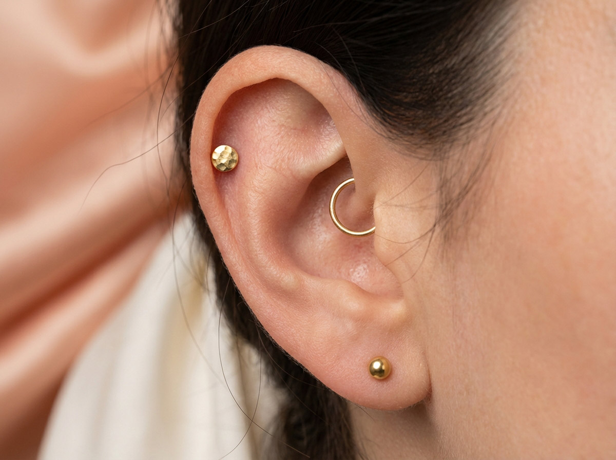 Woman's ear with curated earscape — multiple piercings styled together in gold jewelry 2025