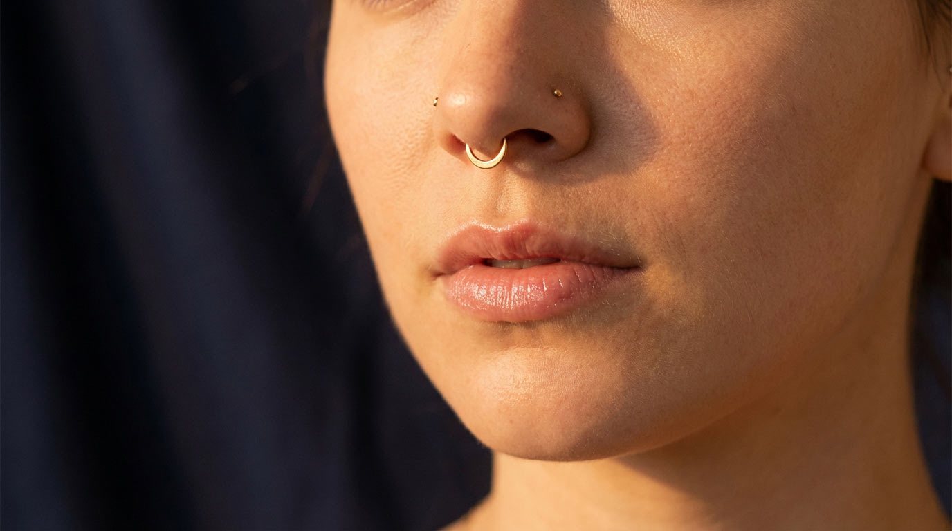 Woman's face with gold septum piercing ring — septum piercing complete guide 2025 showing clicker placement below nasal septum