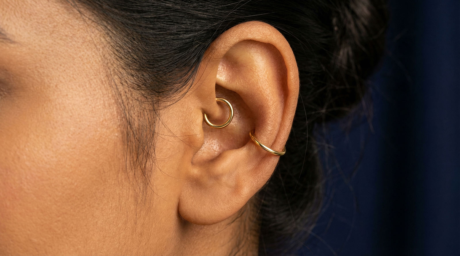 Woman's ear with inner conch piercing and large gold hoop — conch piercing complete guide showing orbital hoop placement wrapping outer ear edge