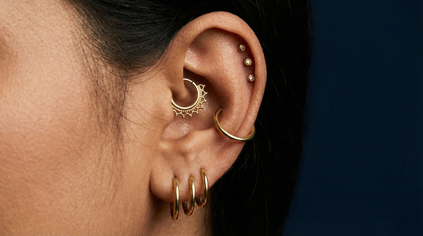 Inner conch vs outer conch piercing comparison — flat-back stud in deep inner conch bowl versus orbital hoop in outer contra conch placement