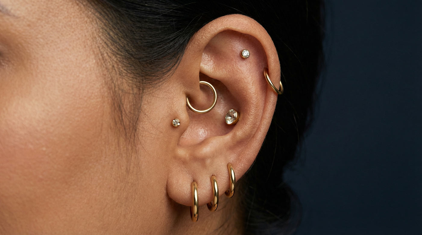 Woman's ear showing fully curated earscape with helix, daith, tragus, conch and stacked lobe piercings in gold titanium — types of ear piercings complete guide