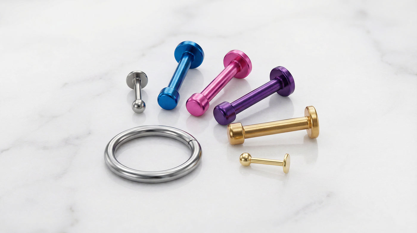 Implant grade titanium ASTM F136 piercing jewelry flatlay on white marble — hypoallergenic nickel-free earrings including flat-back labret studs and seamless hoops